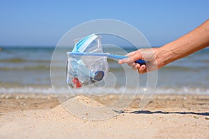 Sieve full of garbage in a female hand on the background of the sea. There is a pile of clean sand under the sieve.