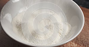 sieving flour with mug sieve on plate closeup