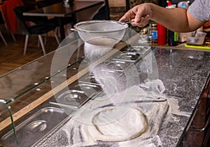 Sift flour by sieve with the flour for beating up dough, pizza. Hands to rub flour. Process of making pizza photo