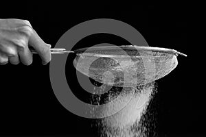 Sifting flour through a sieve on the black background closeup