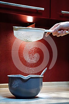 Sifting flour through a sieve into a plastic bowl