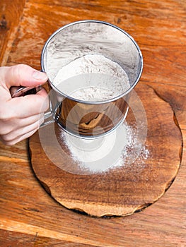 sifting the flour through sifter on wooden board