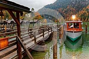 Sightseeing boat parking by a wooden pier at beautiful lakeside in a misty foggy morning on Lake Konigssee