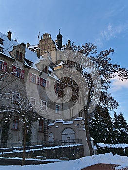 Gate and facade of historic Hohenzollern Castle in winter with snow, bare trees and blue sky.