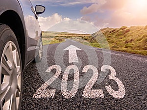 Sign 2023 and directional arrow on small asphalt country road and a side of a car. Travel and explore concept. Warm sunny day, sun