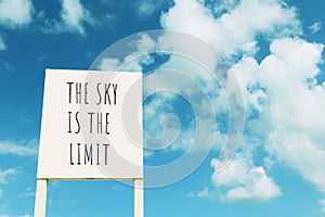 Sign against blue sky with clouds with the text â€“ the sky is the limit
