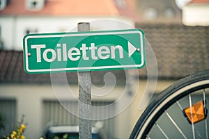 A sign against urban background pointing to the nearest toilet