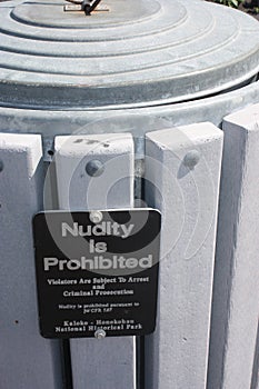 A sign attached to a garbage can prohibiting nudity at Kaloka Honokohau National Historical Park