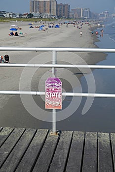 Sign attached to the railing of a wooden pier by the beach says Summer Is A State Of Mind