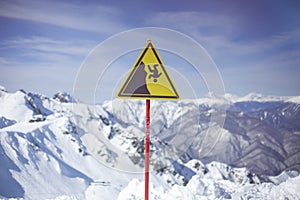 Sign on background of mountains. Sign warning of danger of falling. Triangle on stick. Symbol on yellow background. Carefully
