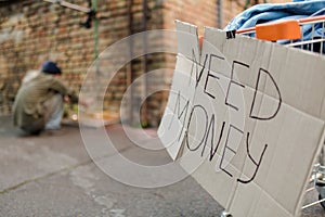 Sign on cardboard need money, homeless man washing hands on backstage.