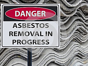 Sign danger asbestos removal in progress and a stack of sheets roof of asbestos.