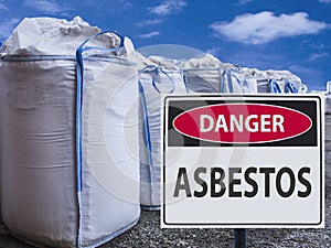 Sign danger asbestos and a stack of big bags of asbestos.