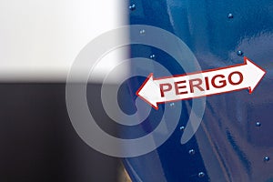 Sign is displayed on a blue background, with the word 'Perigo' written in bold red lettering