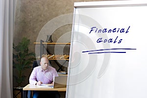 Sign Financial Goals sign on the White Board. Businessman working at work table