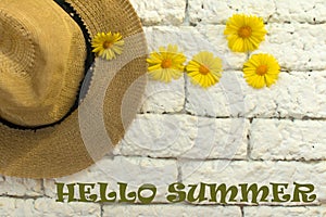 Sign `Hello summer` on a background of white brick wall hat and summer wild flowers