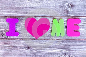 Sign i love me made of colorful letters and a heart on wooden background, self loving concept