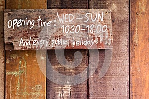 The sign indicates the closing and opening times of shops and locations, it is written in white letters on an old wooden wall
