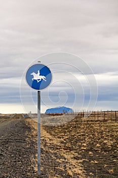 Sign indicates horses with riders ahead on country road, Iceland