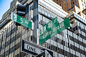 The sign at the intersection of Fifth Avenue and Little Barsil Street, with skyscrapers in the background.
