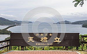 The Sign with Lettering of Amanohashidate, in engl. `Heaven Brigde, Heritage of Japan` with Miyazu Bay and Islands between a gre