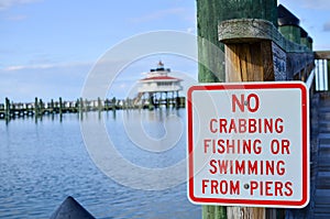 Sign for no crabbing, no fishing and no swimming from the pier. Choptank River Lighthouse in Maryland blurred in background photo