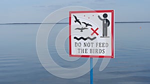 Sign over water to not feed the birds. Do not feed the birds warning sign on water background.