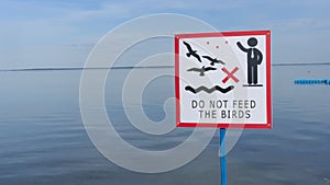 Sign over water to not feed the birds. Do not feed the birds warning sign on water background.