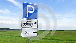 Sign for parking and charging electric vehicles standing near the highway on the background of green field with a forest. Charging