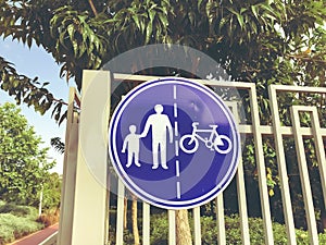Sign for pedestrians and cyclists on a white fence near a road in the park