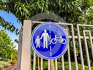 Sign for pedestrians and cyclists on a white fence near a road in the park