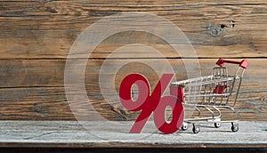 sign percent and shopping cart on wood background