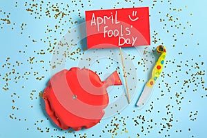 Sign with phrase April Fools` Day, whoopee cushion and party blower on light blue background, flat lay photo