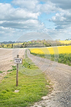 Sign post private track on farmland with trail leading into the distance flanked by fields of crops ploughed and oilseed rape