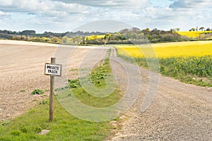 Sign post private track on farmland with trail leading into the distance flanked by fields of crops ploughed and oilseed rape