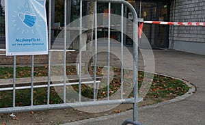 A sign poster in German language saying a face mask is obligatory on school ground, fixed on a metal barrier