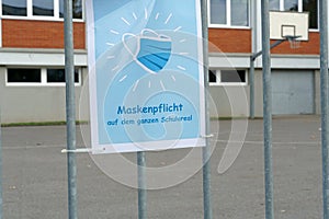 A sign poster on school yard in German language saying: a face mask is obligatory on the whole school ground.