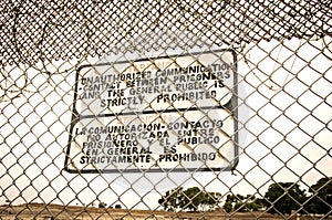 Sign at a prison fence with barbed wire limiting contact with inmates in both english and spanish