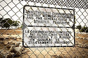 Sign at a prison fence with barbed wire limiting contact with inmates in both english and spanish