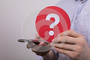 Sign of the question mark made of red paper and smartphone in the hands of a man