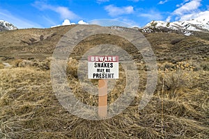 Sign that reads Beware Snakes May Be Present on a grassy mountain