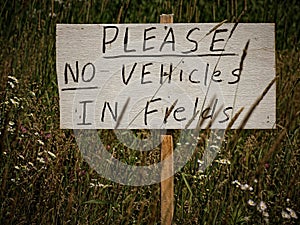 Sign that reads 'Please No Vehicles In Fields' against a backdrop of a lush, vibrant field