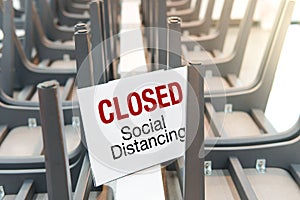 A sign on row of table with upside down chairs on top with `Closed Social Distancing` words.