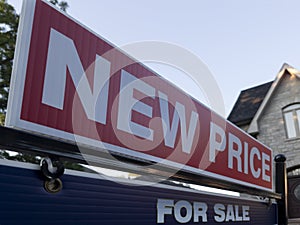 Sign for sale new price by detached house in residential area. Real estate market volatility concept.