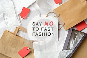 Sign `Say NO to fast fashion` on white paper over shopping bags on table