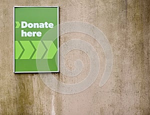 Sign saying `Donate here` against rough worn out concrete wall