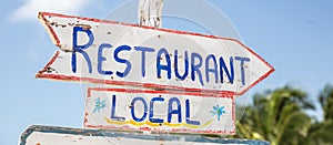 A sign saying Local Restuarant points to the right in a tropical summer destination, written on a rustic wooden white board