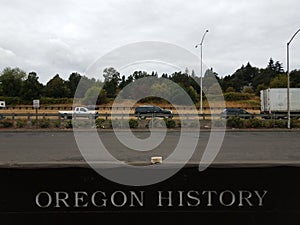 Sign that says Oregon history on side of road with cars