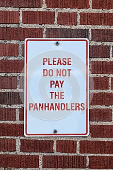 Sign that says please do not pay the panhandlers posted on brick wall - close-up