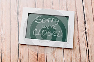 Sign `Sorry, we are closed` on a chalk board with English inscriptions on a wooden background. Closed business